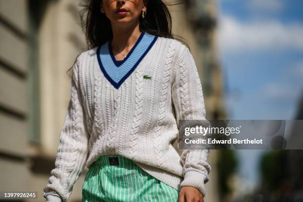 Gabriella Berdugo wears a gold chain pendant necklace, a navy blue t-shirt, a white latte braided wool pullover with a blue V-neck, a mint green and...