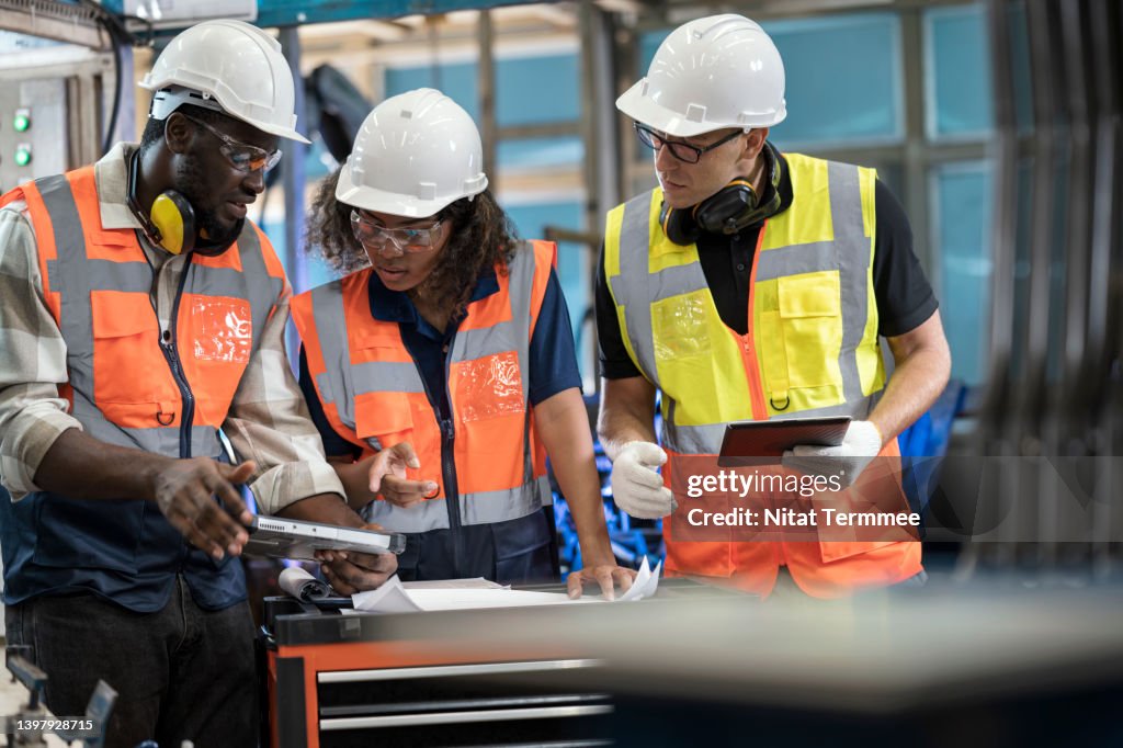 Reduce Manufacturing Waste Solution. Group of Manufacturing Process Engineers having a discussion about welding assembly process improvement to reduce parts defect during production in front of the production line.