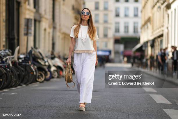 Maria Rosaria Rizzo wears white sunglasses, a white pearls long necklace, a white latte t-shirt with fringed borders, a beige wickers handbag from...