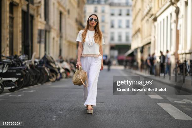 Maria Rosaria Rizzo wears white sunglasses, a white pearls long necklace, a white latte t-shirt with fringed borders, a beige wickers handbag from...