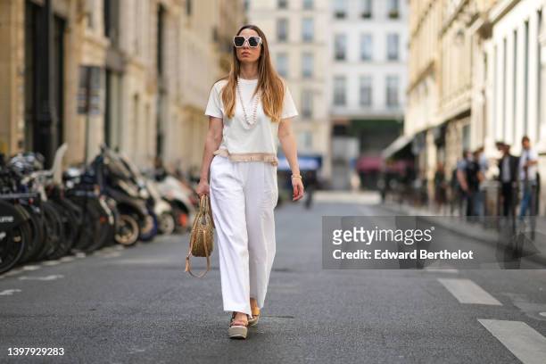 Maria Rosaria Rizzo wears white sunglasses, a white pearls long necklace, a white latte t-shirt with fringed borders, a beige wickers handbag from...