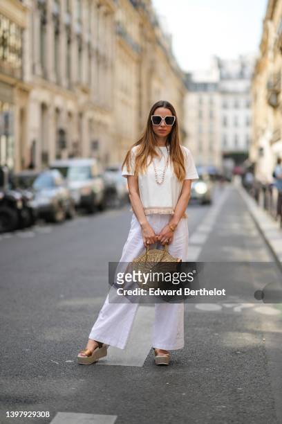 Maria Rosaria Rizzo wears white sunglasses, a white pearls long necklace, a white latte t-shirt with fringed borders, a beige wickers handbag from...
