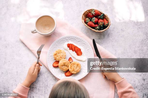 overhead view of caucasian little girl while her breakfast with cottage cheese pancakes and strawberry at home. - plate eating table imagens e fotografias de stock