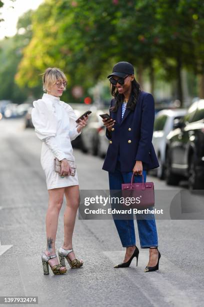 Emy Venturini wears brown sunglasses from Prada, a white puffy long sleeves / belted / short dress from Rotate, a beige and brown print pattern...