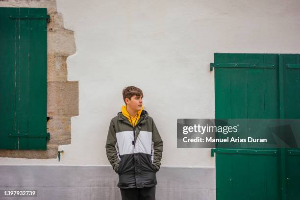 boy dressed in casual clothes, leaning against the wall on a street in a french village. - espelette france photos et images de collection