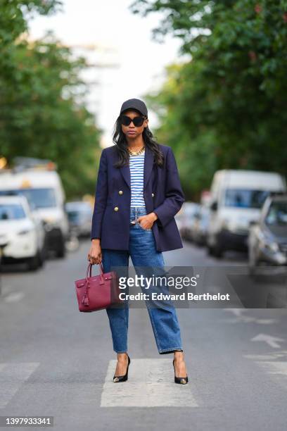 Emilie Joseph wears a black cap from Y3 by Adidas x Yohji Yamamoto, black sunglasses from Gentle Monster, rhinestone earrings, a white and navy blue...