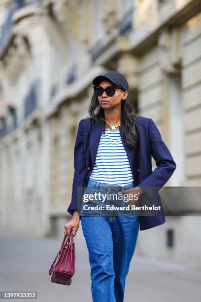 Emilie Joseph wears a black cap from Y3 by Adidas x Yohji Yamamoto, black sunglasses from Gentle Monster, rhinestone earrings, a white and navy blue...