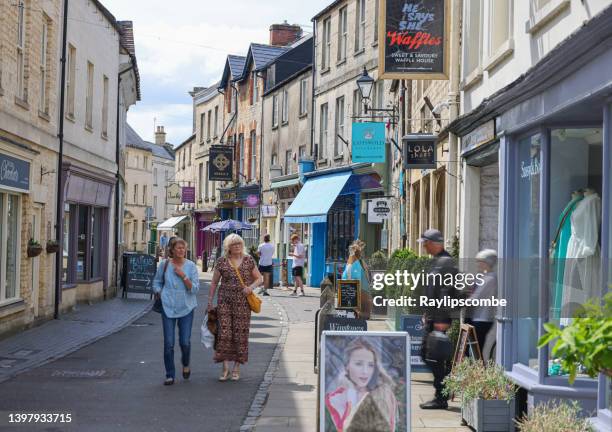 visitors wandering around a quaint small street exploring its small bespoke shops, hidden cafes, deli's and patisseries in the cotswold market town of cirencester in gloucestershire - cirencester stock pictures, royalty-free photos & images