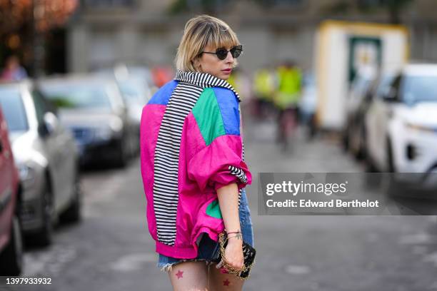 Emy Venturini wears black sunglasses, gold pendant earrings, a black t-shirt from Frankie Shop, a neon pink / blue / neon blue / pale khaki print...