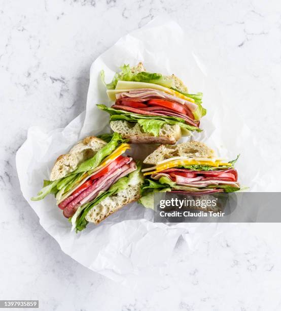 sandwiches with salami, ham, cheese, and tomatoes on parchment paper on white background - delicatessenzaak stockfoto's en -beelden