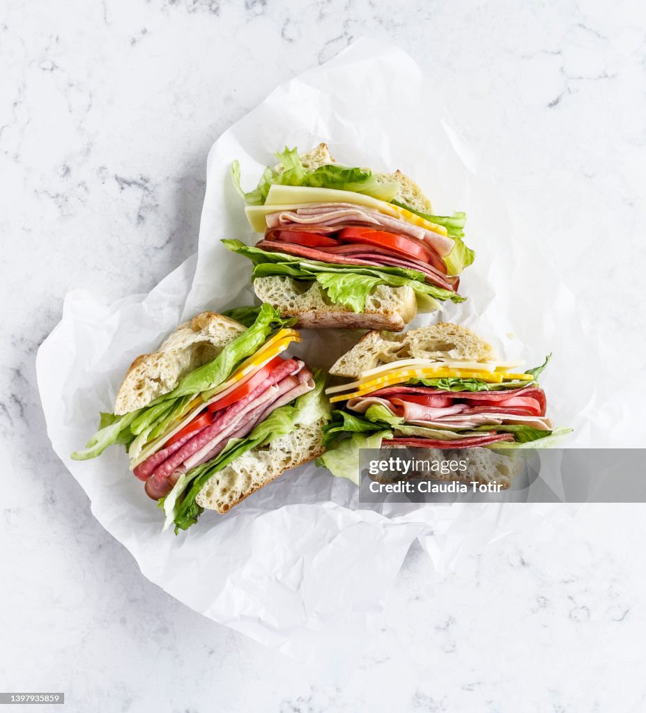 Sandwiches with salami, ham, cheese, and tomatoes on parchment paper on white background