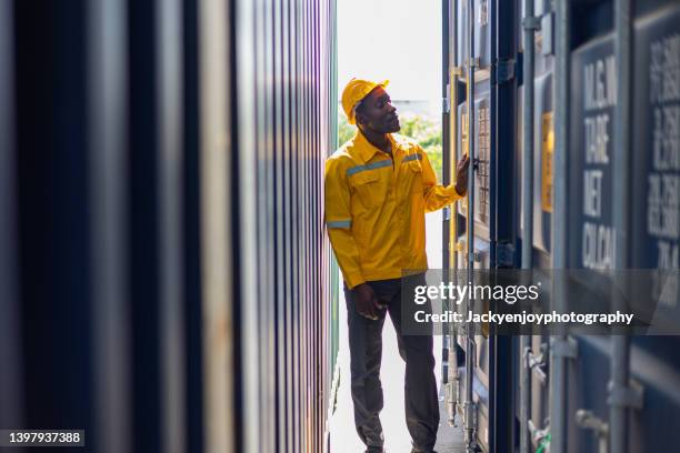 man standing beside cargo container, wearing hard hat - commercial dock stockfoto's en -beelden