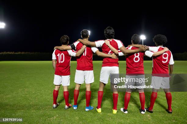 rear view of a team of soccer players hugging and looking at the field - red sports jersey stock pictures, royalty-free photos & images