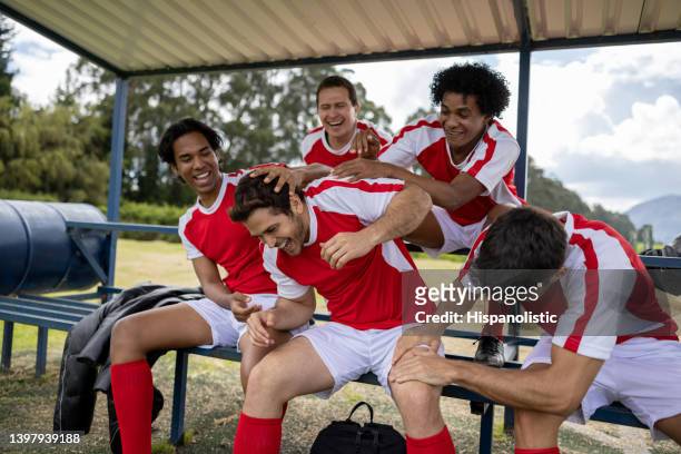 gruppe von fußballspielern, die einen teamkollegen necken und auf der bank lachen - sideline stock-fotos und bilder