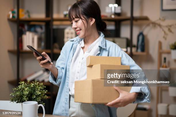 cheerful young woman with smart phone, receiving a parcel - woman online shopping stock-fotos und bilder