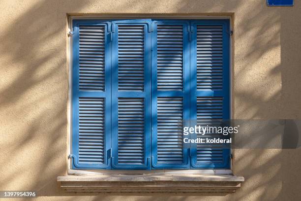 closed blue wooden jalousie window on camel colored wall shaded by trees - cannes building stock pictures, royalty-free photos & images