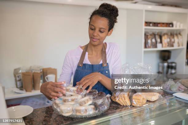 female afro-american entrepreneur  arranging tray full of alfajores de dulce de leche at patisserie - alfajor stockfoto's en -beelden