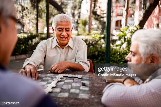 three senior men sitting in the park and playing domino - dominoes stock pictures, royalty-free photos & images