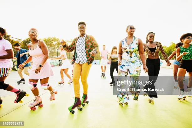 wide shot of group of smiling friends roller skating in unison in park - rollerskates foto e immagini stock