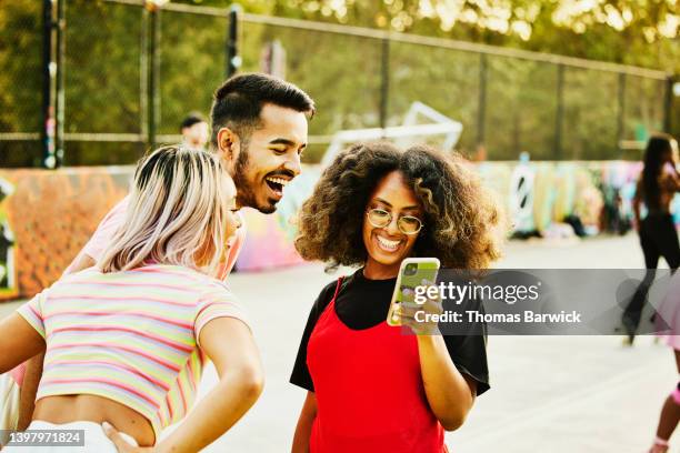 medium shot of friends looking at photo on smart phone while roller skating - medium group of people fotografías e imágenes de stock