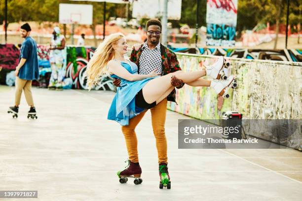 Wide shot of smiling man carrying friend while roller skating in park