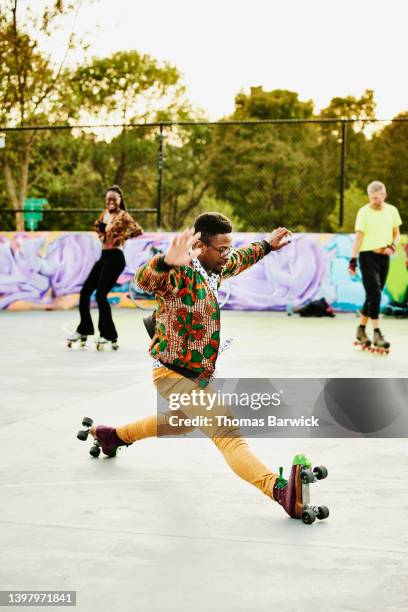 wide shot of man doing splits while roller skating with friends in park - split acrobatiek stockfoto's en -beelden