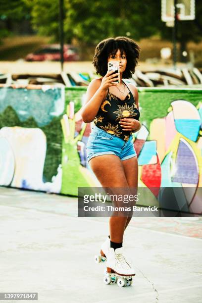 wide shot of woman taking video on smart phone while roller skating in park - black shorts photos et images de collection