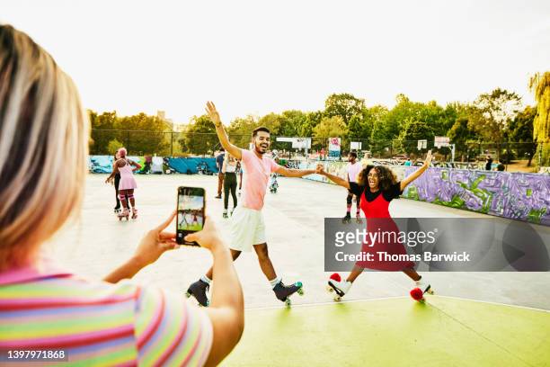 wide shot of friends holding hands and balancing on roller skates - white shorts stock pictures, royalty-free photos & images
