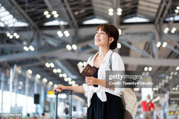 cheerful young asian woman standing in front of the flight schedule in the airport departure hall - leaving card stock pictures, royalty-free photos & images