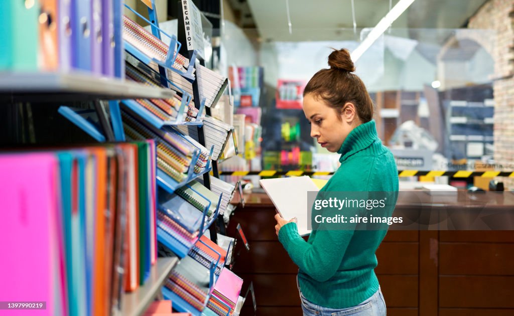 Woman looking notebooks on the bookshelf at the stationery shop. Shop and office or school supplies concept.