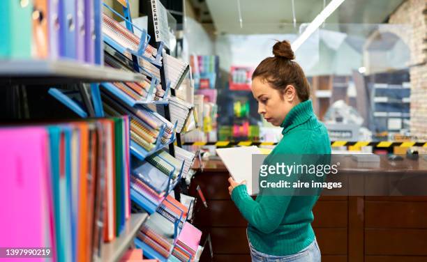 woman looking notebooks on the bookshelf at the stationery shop. shop and office or school supplies concept. - utiles escolares fotografías e imágenes de stock
