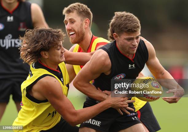 Brayden Ham of the Bombers is challenged by Tex Wanganeen and Dyson Heppell during an Essendon Bombers AFL training session at The Hangar on May 19,...