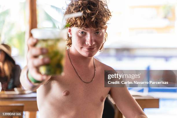 young man toasting to the camera with a cocktail on a bar in the beach - hunky guy on beach stock pictures, royalty-free photos & images