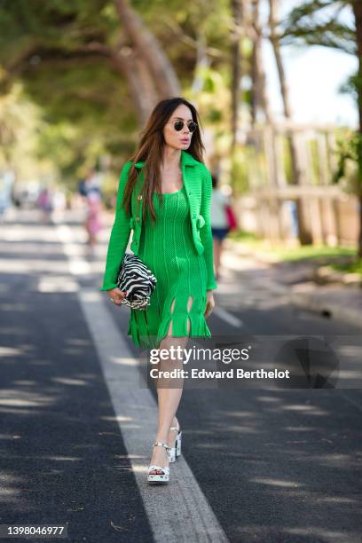 Sira Pevida wears black circle sunglasses, a green cut-out details / V-neck / short dress, a matching green tweed cropped jacket, a black and white...