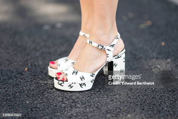 Sira Pevida wears white with black CC logo print pattern block heels sandals from Chanel, on May 18, 2022 in Cannes, France.