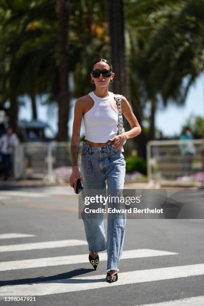Alexandra Guerain wears black futurist sunglasses from Chanel, gold earrings, a white halter-neck / cropped tank-top, a white shiny leather nailed /...