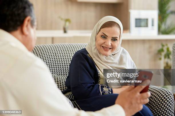 mature saudi couple looking at photos on smart phone - saudi arabia women stock pictures, royalty-free photos & images