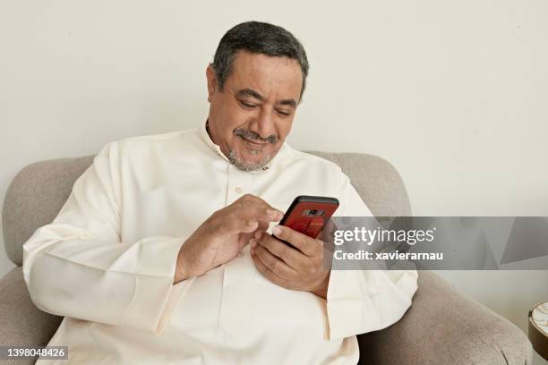 mature saudi man relaxing at home with smart phone - arabian peninsula stock pictures, royalty-free photos & images