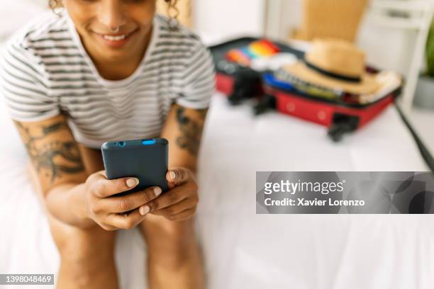 smiling young tourist woman using mobile phone while preparing summer suitcase before going on vacation - the package tour stock pictures, royalty-free photos & images