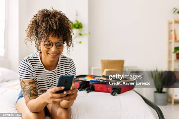 happy young african american woman booking a hotel room while packing her summer suitcase for holidays - black room photos et images de collection