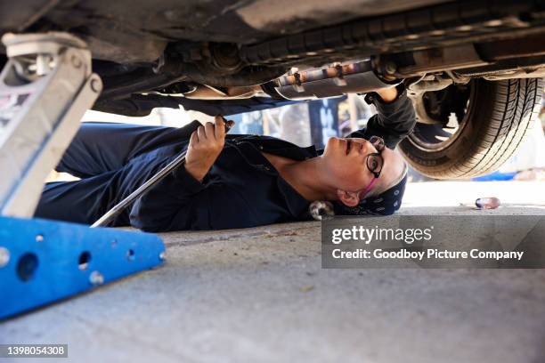 young female mechanic working on the underside of a car - car underside stock pictures, royalty-free photos & images