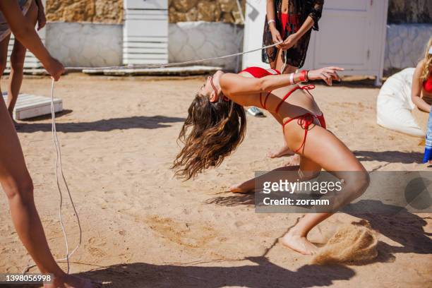 junge frau im roten bikini, die sich für eine limbo-tanz-challenge am sandstrand nach hinten beugt - limbo stock-fotos und bilder