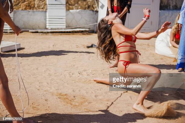 mujer joven en bikini rojo inclinándose hacia atrás y bailando en el limbo en la playa de arena con amigos - limbo blanco fotografías e imágenes de stock