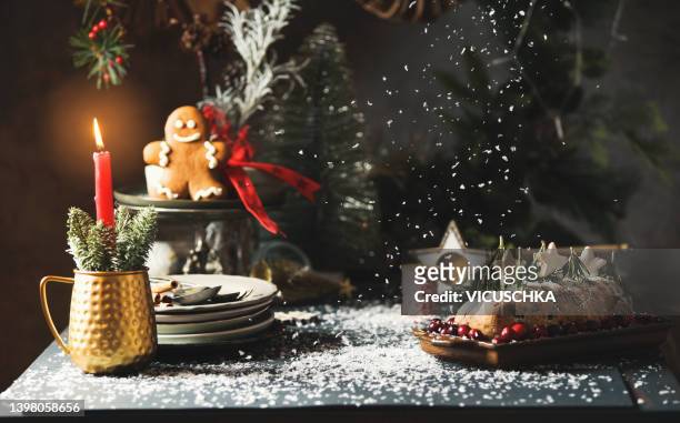 christmas still life with traditional german winter cake stollen , candle, plates, gingerbread men, fir green and snow at dark kitchen table - christmas still life stock-fotos und bilder