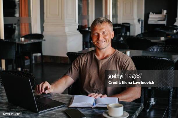 portrait of a man with a laptop in a cafe. a man of european appearance - a freelancer. man working remotely, smiling and looking at camera - eastern european descent stock pictures, royalty-free photos & images