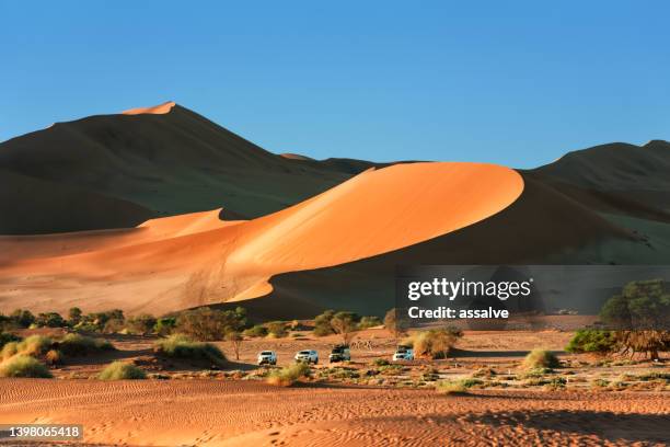 four off-road vehicles parked in front of the sand dunes in sossusvlei, namibia - sossusvlei stock pictures, royalty-free photos & images