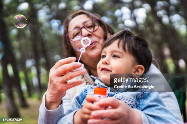 little boy and his grandmother playing together at picnic - child blowing bubbles stockfoto's en -beelden