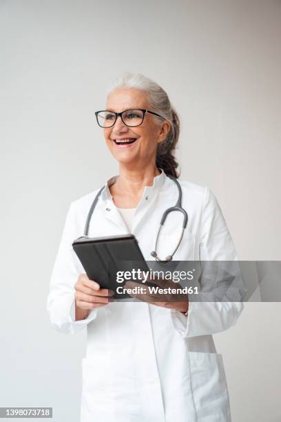 happy senior doctor with tablet pc standing against white background - westend 61 fotografías e imágenes de stock