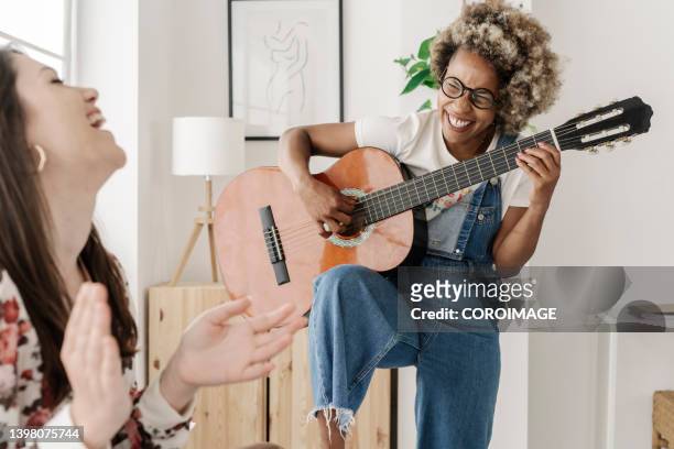 young female couple playing guitar and laughing in the bedroom. - playing guitar stock pictures, royalty-free photos & images