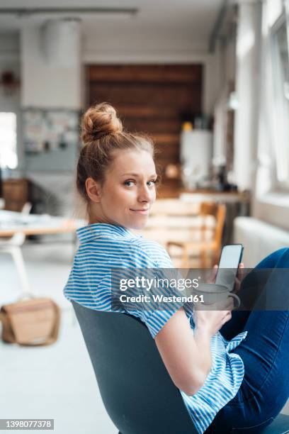 businesswoman with drink and smart phone sitting on chair at home - regarder par dessus son épaule photos et images de collection